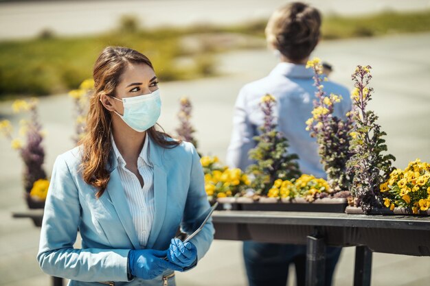 Joven mujer de negocios con máscara protectora en la cara y tableta digital en la mano va a trabajar durante la pandemia de COVID 19.