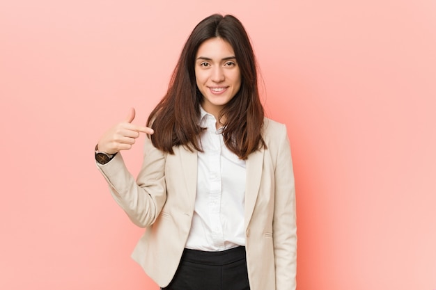 Joven mujer de negocios morena persona contrapink señalando por camisa handa, orgulloso y confiado