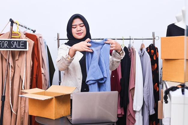 Joven mujer de negocios musulmana propietaria de SME en línea usando una computadora portátil recibe un pedido del cliente con un paquete