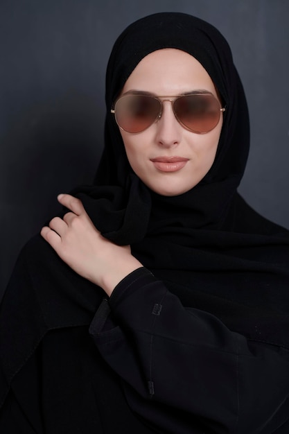 Joven mujer de negocios musulmana con ropa tradicional o abaya y gafas de sol posando frente a una pizarra negra. Mujer árabe que representa el estilo de vida árabe moderno, la moda islámica y Ramadan kareem conc