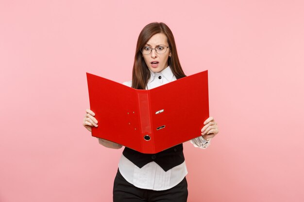 Joven mujer de negocios preocupada en vasos mantenga mirando en carpeta roja para documentos documentos aislado sobre fondo rosa pastel. Jefa. Concepto de riqueza de carrera de logro. Copie el espacio para publicidad.