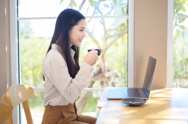 Una joven mujer de negocios que trabaja con su computadora portátil en la cafetería.