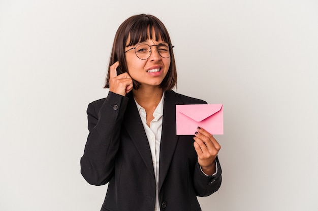 Joven mujer de negocios de raza mixta sosteniendo una carta aislada sobre fondo blanco cubriendo los oídos con las manos.