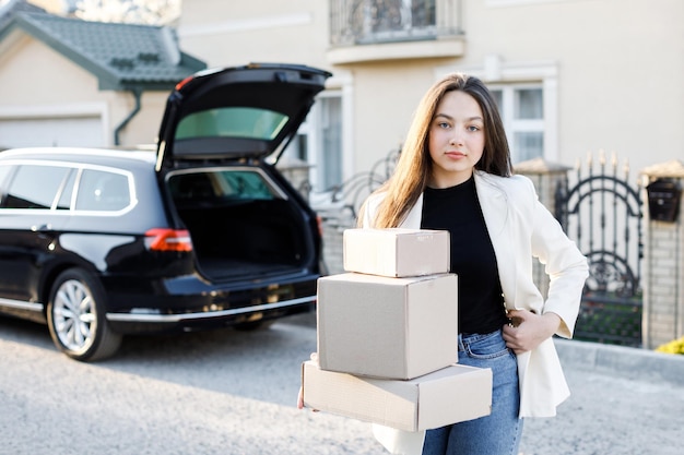 Joven mujer de negocios recogiendo paquetes del maletero de un coche que vuelve a casa en coche Concepto de comprar productos en línea y entregarlos a casa