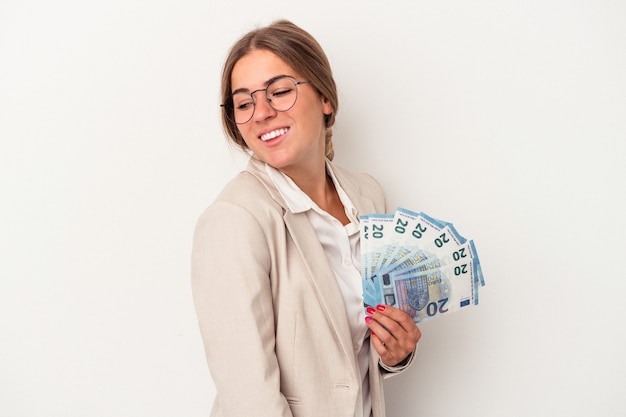 Joven mujer de negocios rusa sosteniendo billetes aislados sobre fondo blanco mira a un lado sonriente, alegre y agradable.