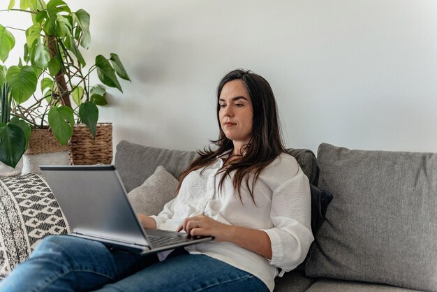 Joven mujer de negocios sentada en el sofá usando una computadora portátil