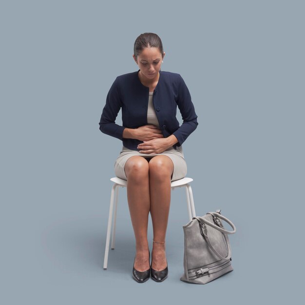Joven mujer de negocios sentada y tocando su estómago está teniendo dolor abdominal