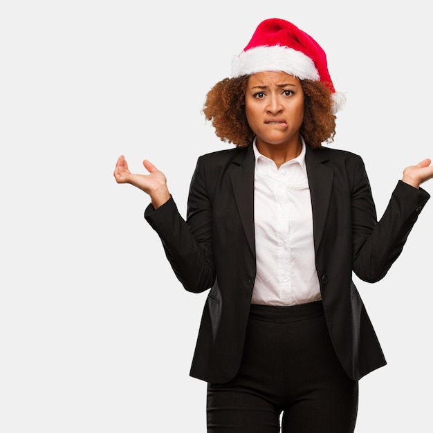 Joven mujer de negocios con un sombrero de santa chirstmas confundido y dudoso