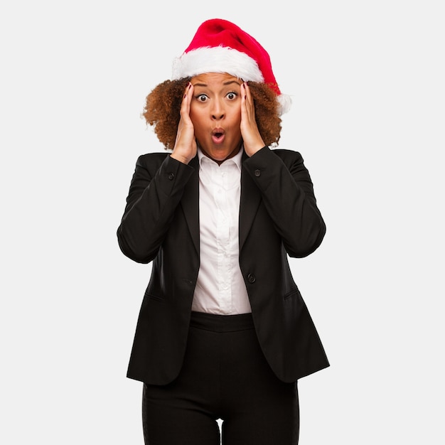 Joven mujer de negocios con un sombrero de santa chirstmas sorprendida y sorprendida