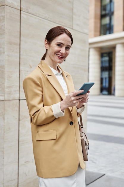 Joven mujer de negocios sonriente con teléfono inteligente de pie junto a la columna