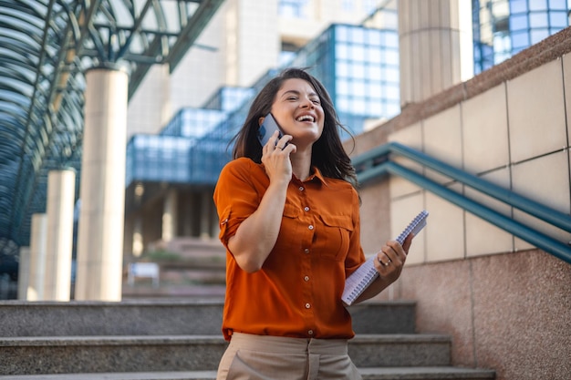 Una joven mujer de negocios sonriente con traje de pie en una escalera mecánica urbana usando aplicaciones en el teléfono celular leyendo noticias en la conexión rápida del teléfono inteligente revisando aplicaciones móviles al aire libre