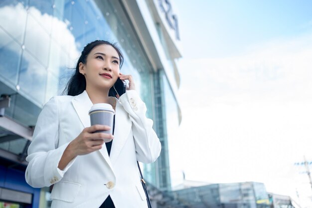 Foto joven mujer de negocios con una taza de café caliente y usando un teléfono inteligente mientras camina por la ciudad