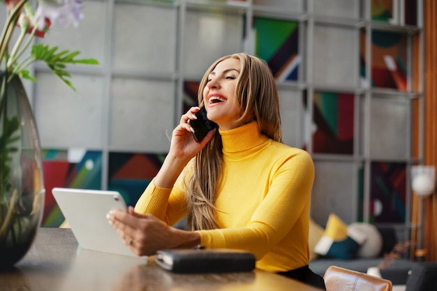 Foto una joven mujer de negocios trabaja en una computadora y habla por teléfono en casa. negocios en línea, trabajo en línea.