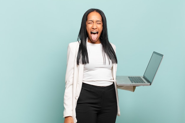 Joven mujer negra con actitud alegre, despreocupada, rebelde, bromeando y sacando la lengua, divirtiéndose. concepto de laptop