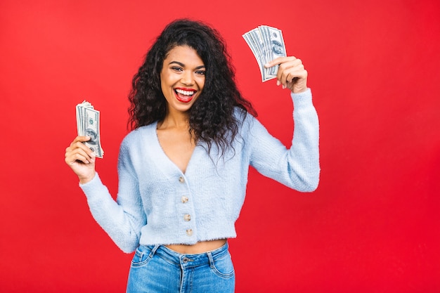 Joven mujer negra afroamericana sosteniendo dinero aislado sobre fondo rojo.