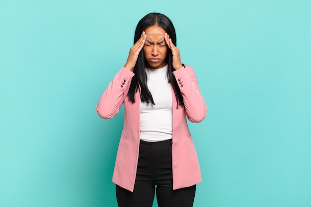 Joven mujer negra con aspecto estresado y frustrado, trabajando bajo presión con dolor de cabeza y preocupado por problemas