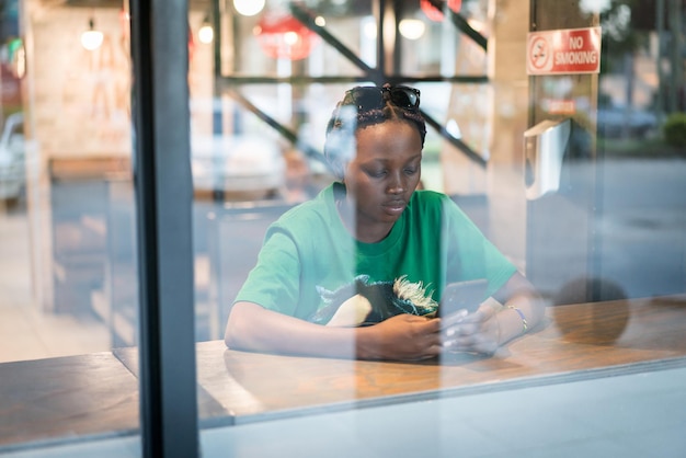 Joven mujer negra auténtica sentada con teléfono en la cafetería de la ciudad por la noche