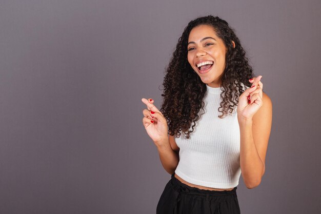 Joven mujer negra brasileña signo de suerte con los dedos cruzados deseando