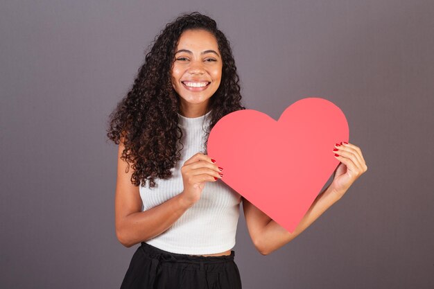 Joven mujer negra brasileña sosteniendo una foto publicitaria de un cartel en forma de corazón