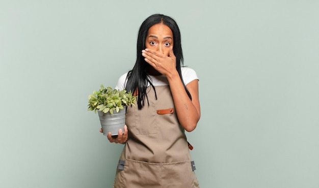 Joven mujer negra cubriendo la boca con las manos con una expresión de sorpresa y sorpresa, manteniendo un secreto o diciendo uy. concepto de jardinero