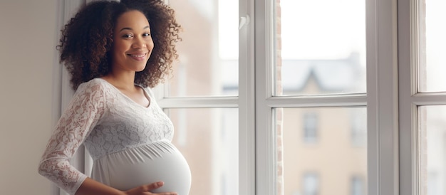 Joven mujer negra embarazada sonriendo y mirando el espacio vacío disfrutando de su embarazo cerca de una ventana en casa