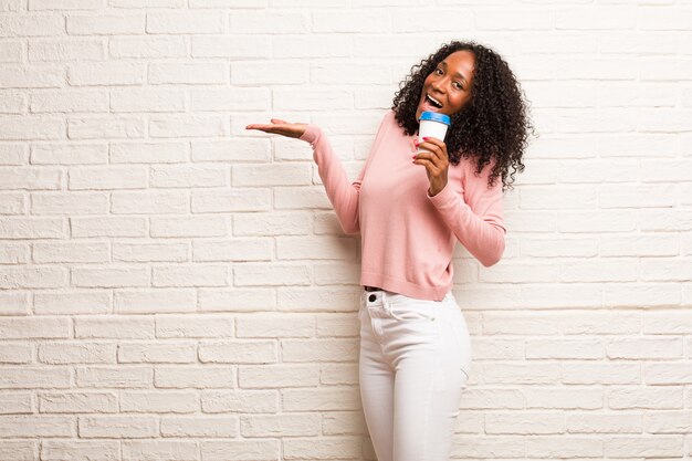 Joven mujer negra gritando feliz, sorprendida por una oferta o una promoción, boquiabierta, saltando y orgullosa