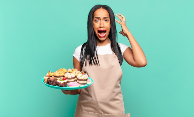 Joven mujer negra gritando con las manos en alto, sintiéndose furiosa, frustrada, estresada y molesta. concepto de chef de panadería