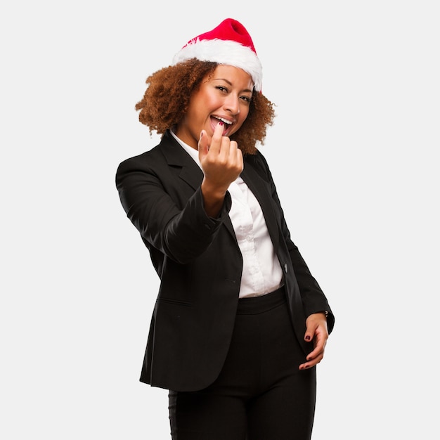 Joven mujer negra de negocios con un sombrero de santa chirstmas invitando a venir