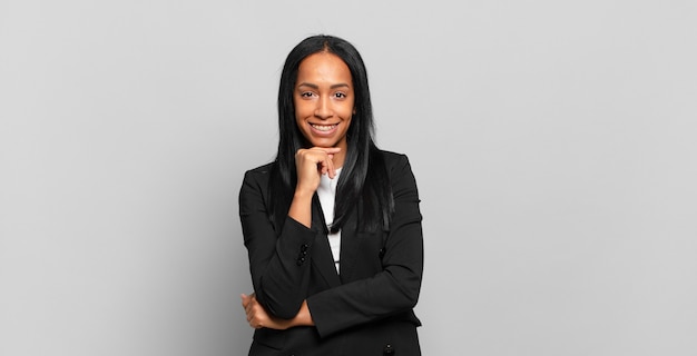 Joven mujer negra que parece feliz y sonriente con la mano en la barbilla, preguntándose o haciendo una pregunta, comparando opciones. concepto de negocio