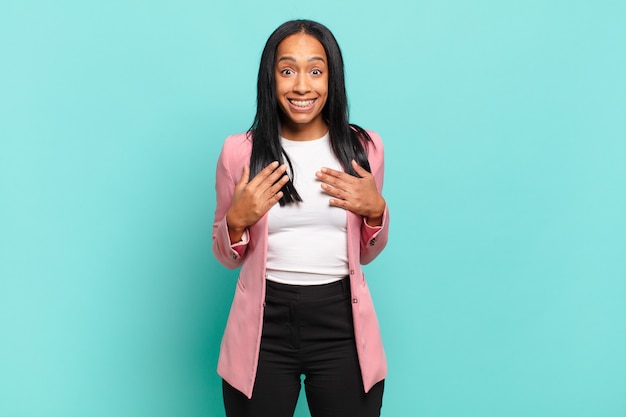 Joven mujer negra que parece feliz, sorprendida, orgullosa y emocionada, apuntando a sí misma. concepto de negocio