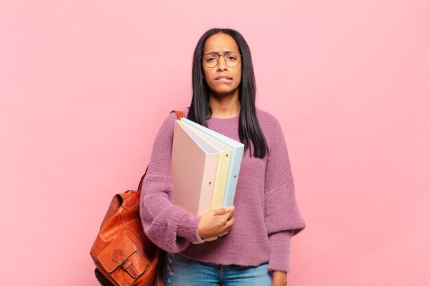 Joven mujer negra que parece perpleja y confundida, mordiéndose el labio con un gesto nervioso, sin saber la respuesta al problema. concepto de estudiante