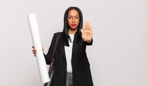 Joven mujer negra que parece seria, severa, disgustada y enojada mostrando la palma abierta haciendo gesto de parada. concepto de arquitecto