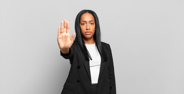 Joven mujer negra que parece seria, severa, disgustada y enojada mostrando la palma abierta haciendo gesto de parada. concepto de negocio