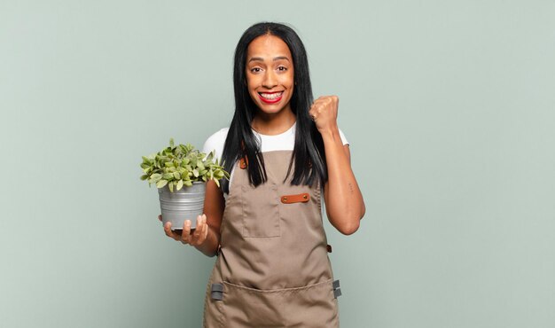 Joven mujer negra que se siente conmocionada, emocionada y feliz, riendo y celebrando el éxito, diciendo ¡guau !. concepto de jardinero