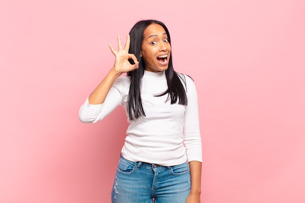 Joven mujer negra que se siente exitosa y satisfecha, sonriendo con la boca abierta, haciendo un buen signo con la mano