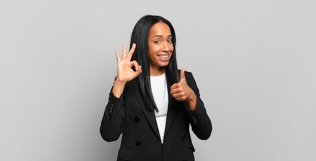 Joven mujer negra que se siente feliz, asombrada, satisfecha y sorprendida, mostrando gestos bien y pulgares arriba, sonriendo. concepto de negocio