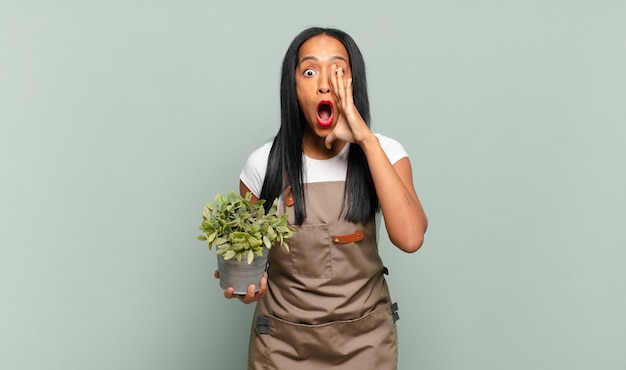 Joven mujer negra que se siente feliz, emocionada y positiva, dando un gran grito con las manos al lado de la boca, gritando. concepto de jardinero