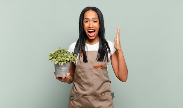 Joven mujer negra que se siente feliz, emocionada, sorprendida o consternada, sonriendo y asombrada por algo increíble. concepto de jardinero