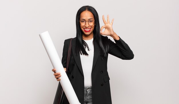 Joven mujer negra que se siente feliz, relajada y satisfecha, mostrando aprobación con gesto bien, sonriendo. concepto de arquitecto