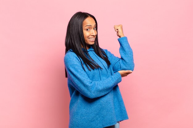 Joven mujer negra que se siente feliz, satisfecha y poderosa, flexionando el ajuste y los bíceps musculosos