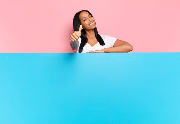 Joven mujer negra que se siente orgullosa, despreocupada, segura y feliz, sonriendo positivamente con los pulgares hacia arriba. concepto de espacio de copia