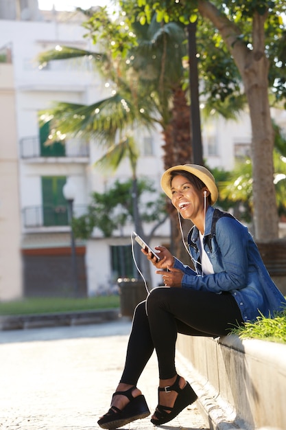 Joven mujer negra riendo y escuchando música en el teléfono celular