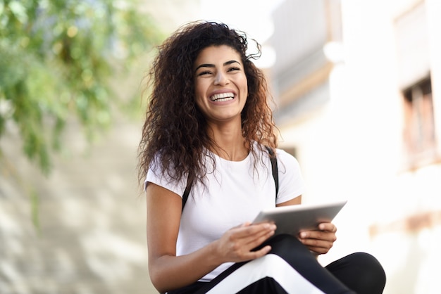 Joven mujer negra en ropa deportiva usando tableta digital al aire libre