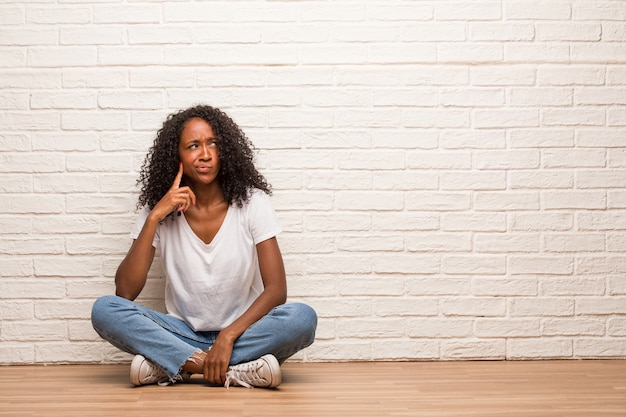Joven mujer negra sentada en un piso de madera dudando y confundida