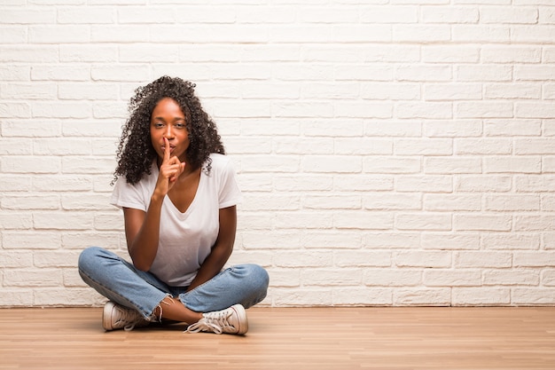 Joven mujer negra sentada en el piso de madera guardando un secreto o pidiendo silencio