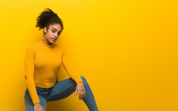 Joven mujer negra sentada sobre un muro naranja