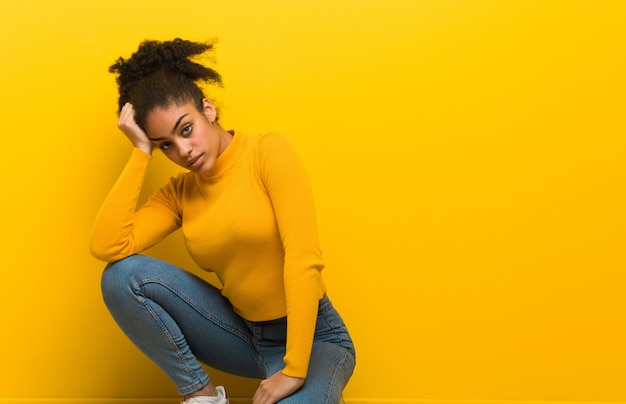 Joven mujer negra sentada sobre una pared naranja