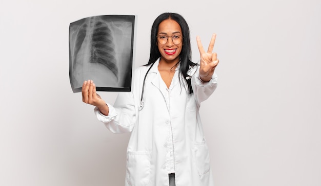 Foto joven mujer negra sonriendo y luciendo feliz, despreocupada y positiva, gesticulando victoria o paz con una mano. concepto médico