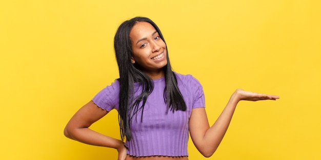 Joven mujer negra sonriendo, sintiéndose confiada, exitosa y feliz, mostrando concepto o idea en el espacio de la copia en el lateral