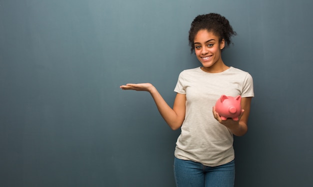 Joven mujer negra sosteniendo algo con la mano. Ella está sosteniendo una alcancía.